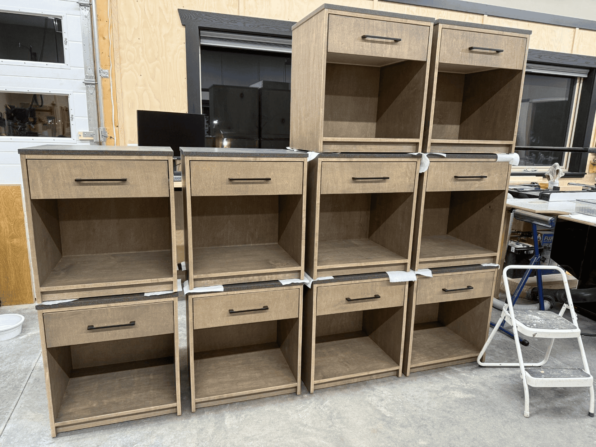 Custom wood cabinetry display featuring multiple units with drawers and open shelves, showcasing quality craftsmanship by Beaver Custom Builds in a workshop setting.