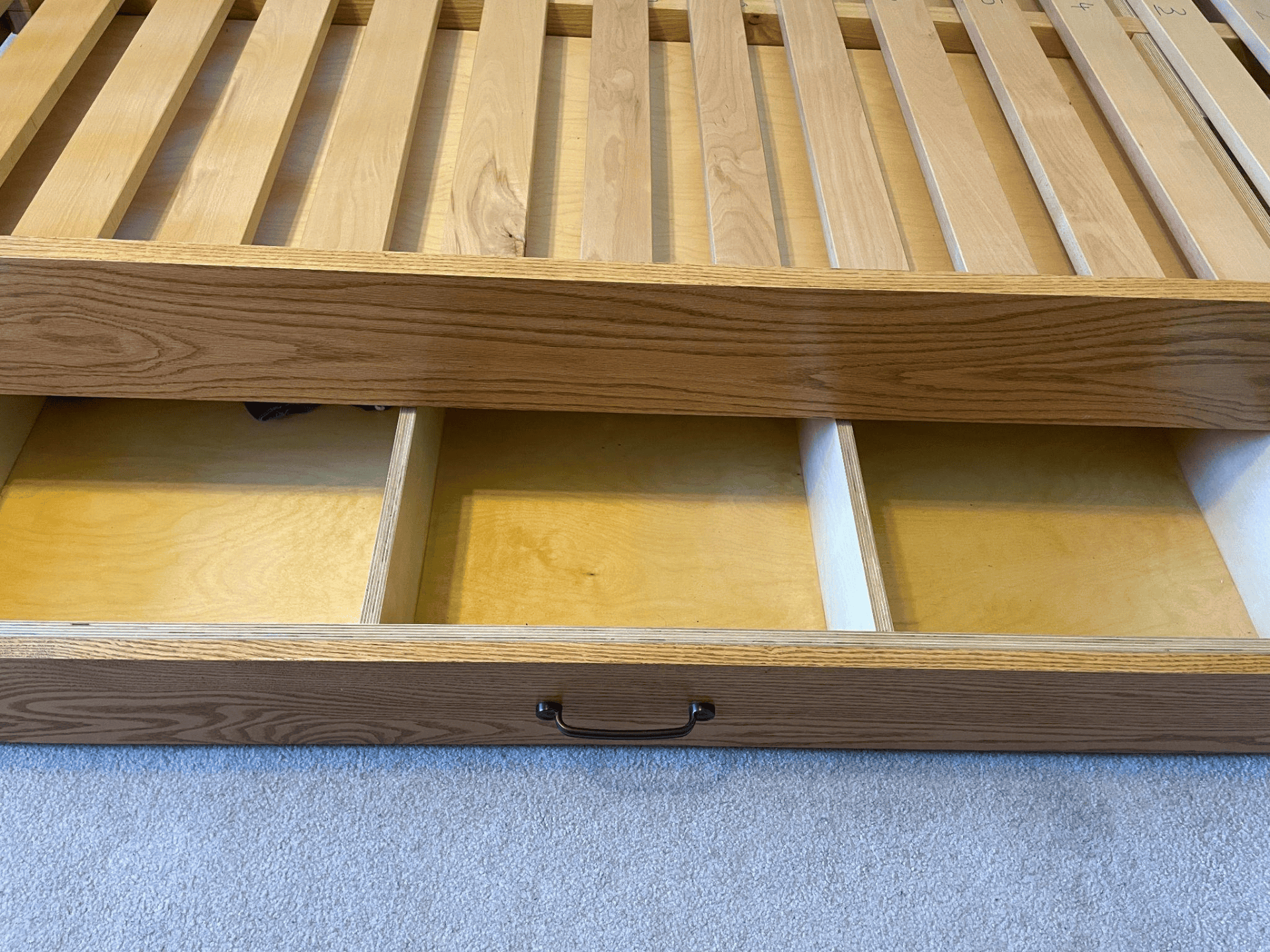 Custom wooden bed frame with slatted design and open storage drawers, showcasing quality craftsmanship by Beaver Custom Builds.