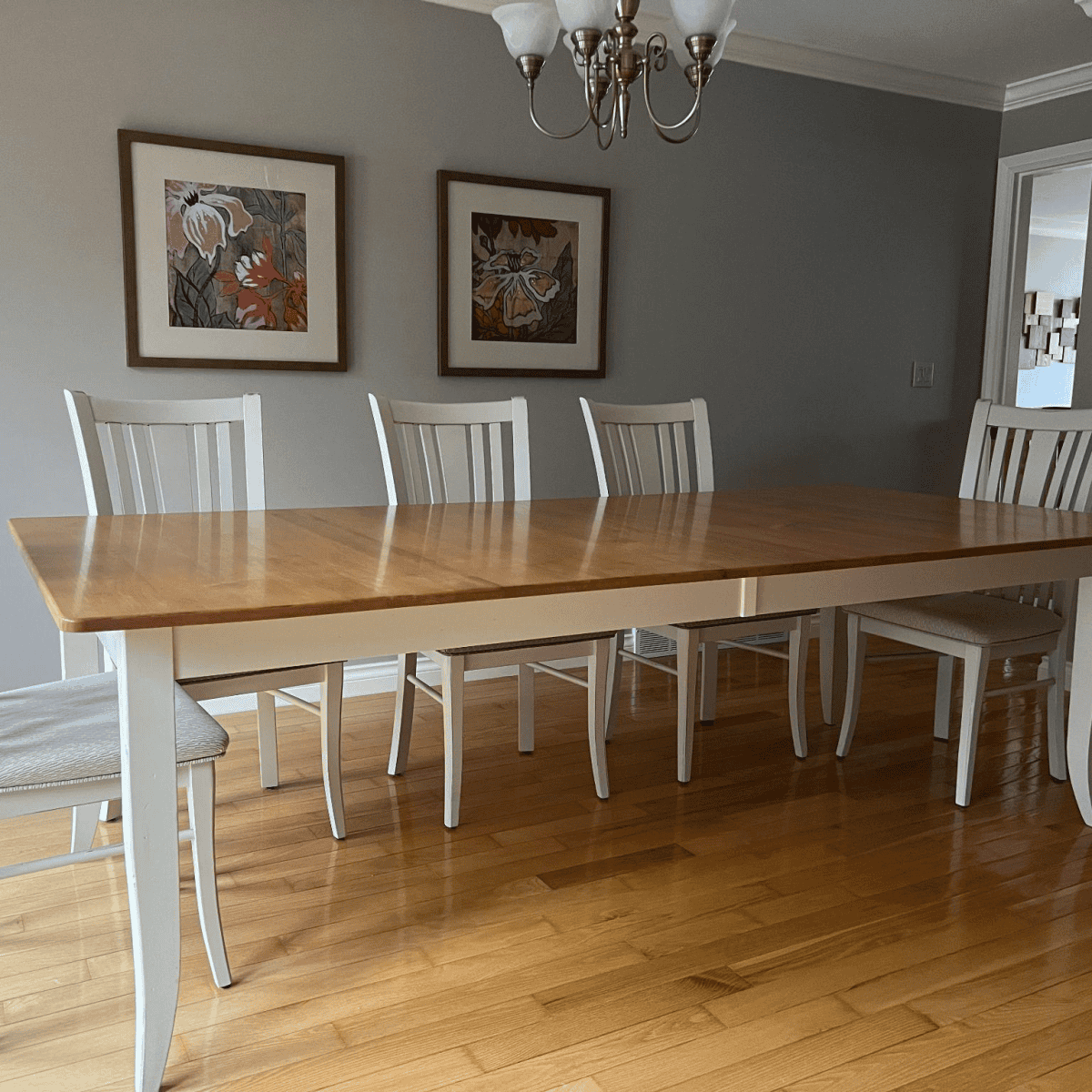 Custom wooden dining table with white chairs, framed artwork on the wall, showcasing quality craftsmanship by Beaver Custom Builds.