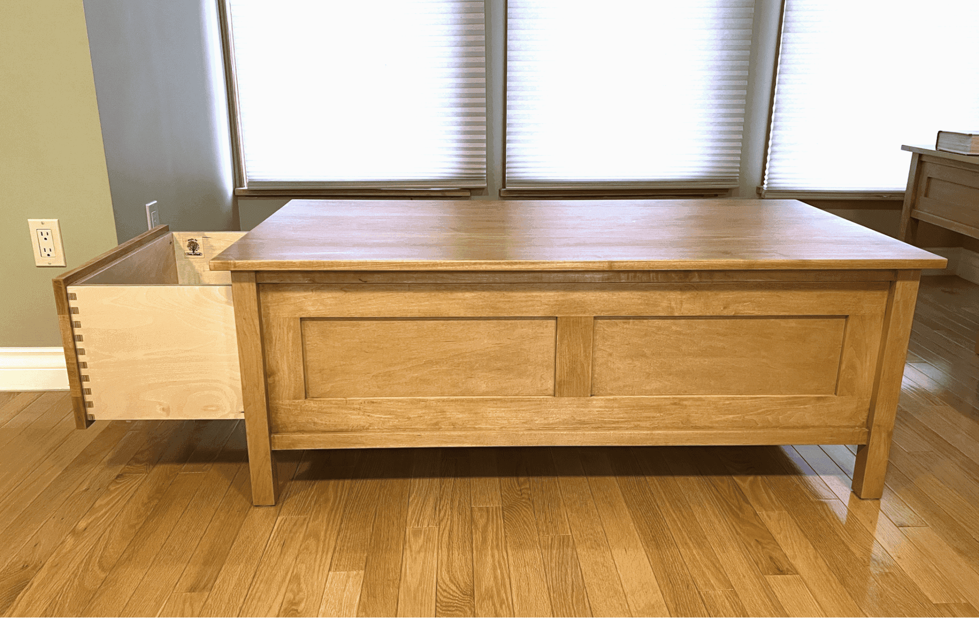 Custom wooden coffee table with an open drawer, showcasing quality craftsmanship and attention to detail, set in a well-lit interior space.