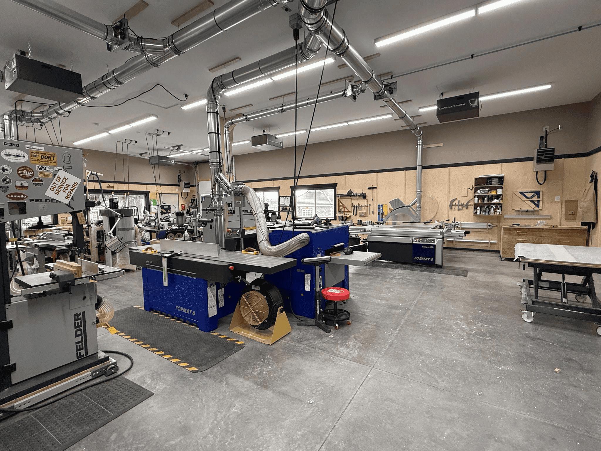 Woodworking shop interior featuring various machinery, including a blue Format 4 table saw, Felder equipment, and workstations, emphasizing custom woodworking capabilities.