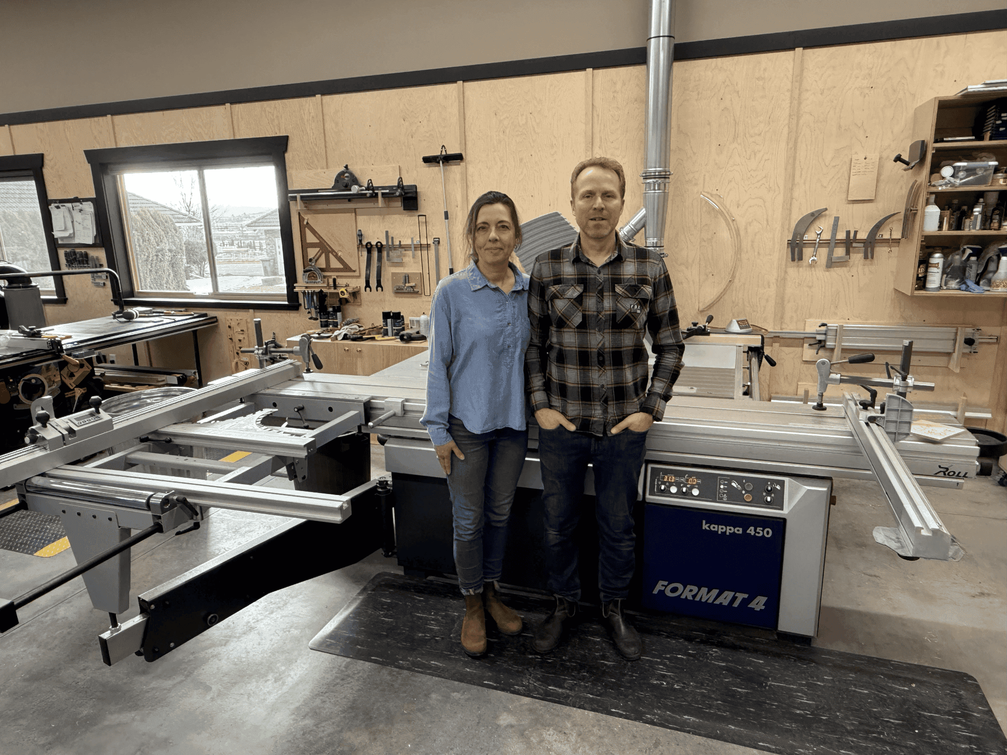 Peter and Gabriele standing in Beaver Custom Builds workshop beside a FORMAT 4 kappa 450 woodworking machine, showcasing their dedication to quality craftsmanship in custom furniture.