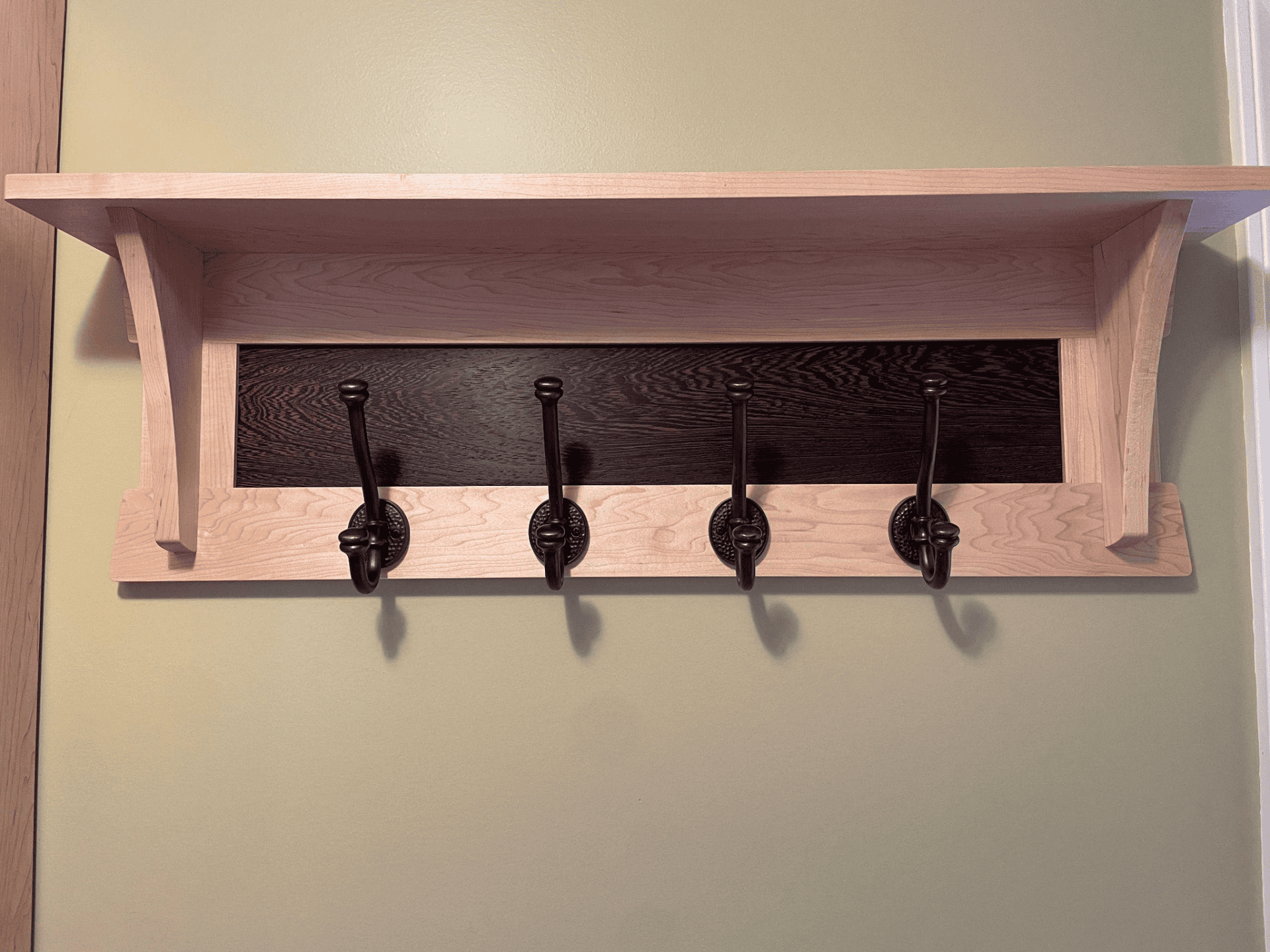 Custom wood wall-mounted shelf with hooks, featuring a light maple finish and dark wood panel, showcasing craftsmanship by Beaver Custom Builds.