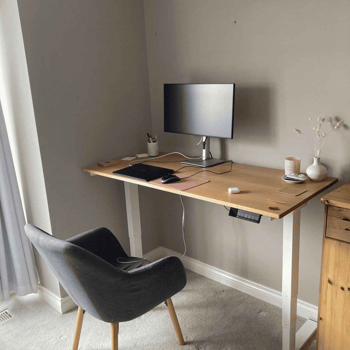 Custom wooden desk with monitor, keyboard, and accessories, accompanied by a comfortable chair in a well-lit workspace.